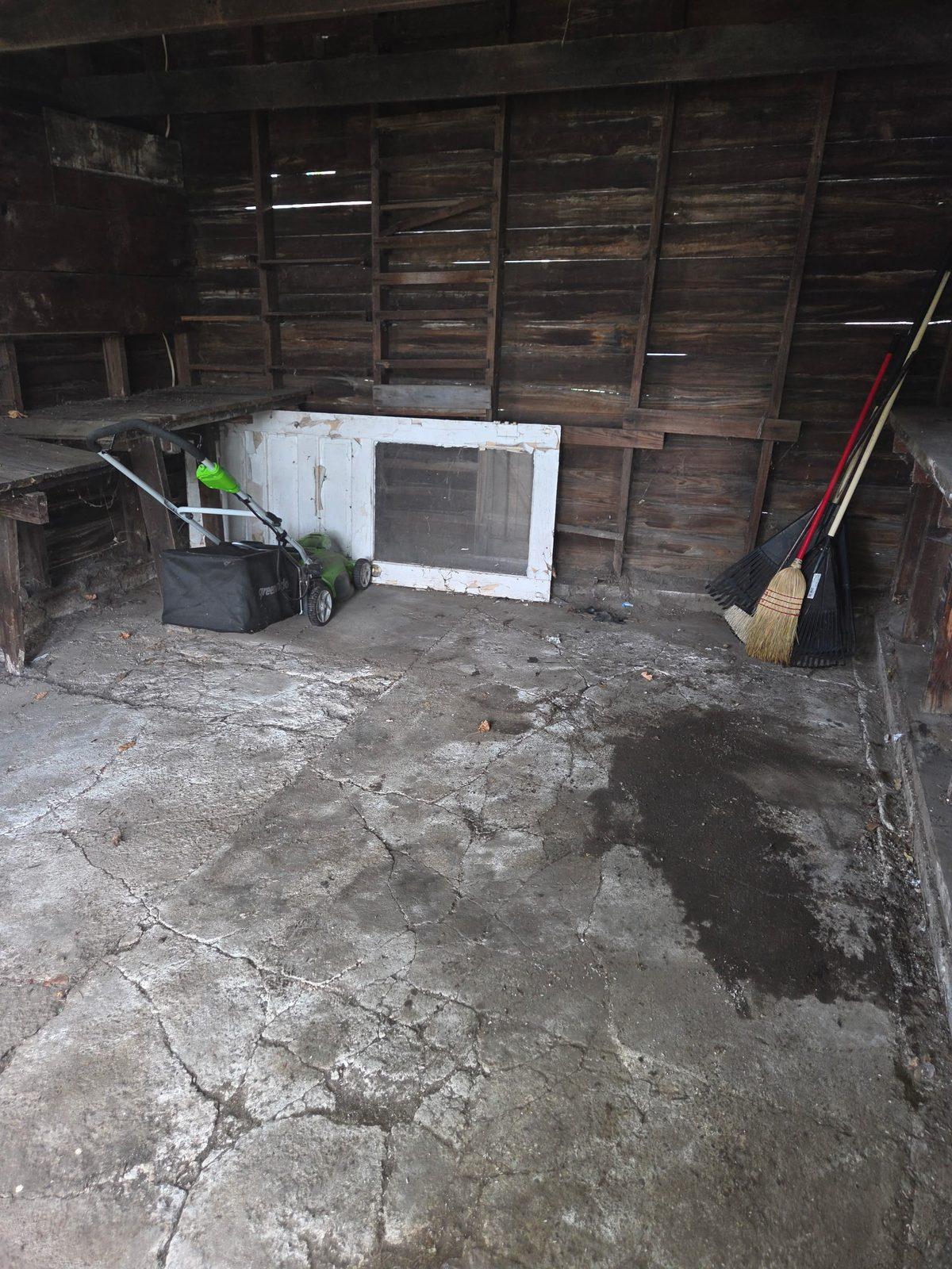 Emptied garage floor swept clean with only a mower and yard tools left standing