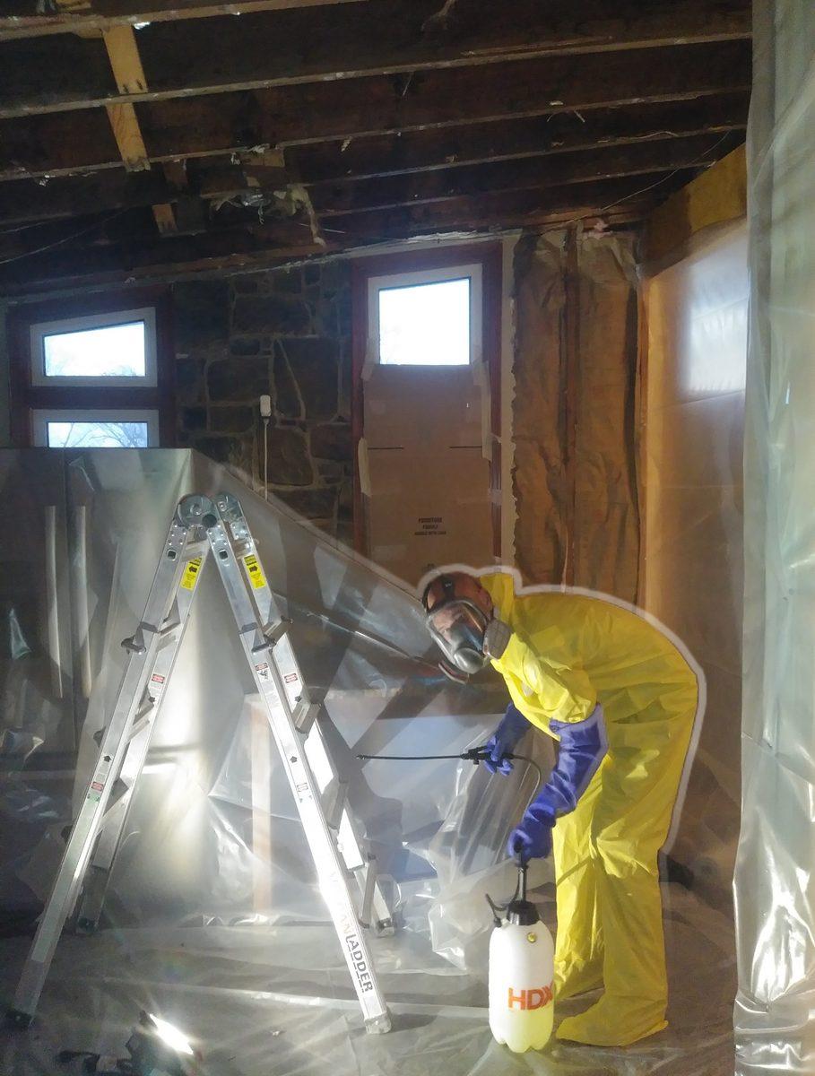 Work area sealed in plastic sheeting with a tradesman in a protective suit and respirator