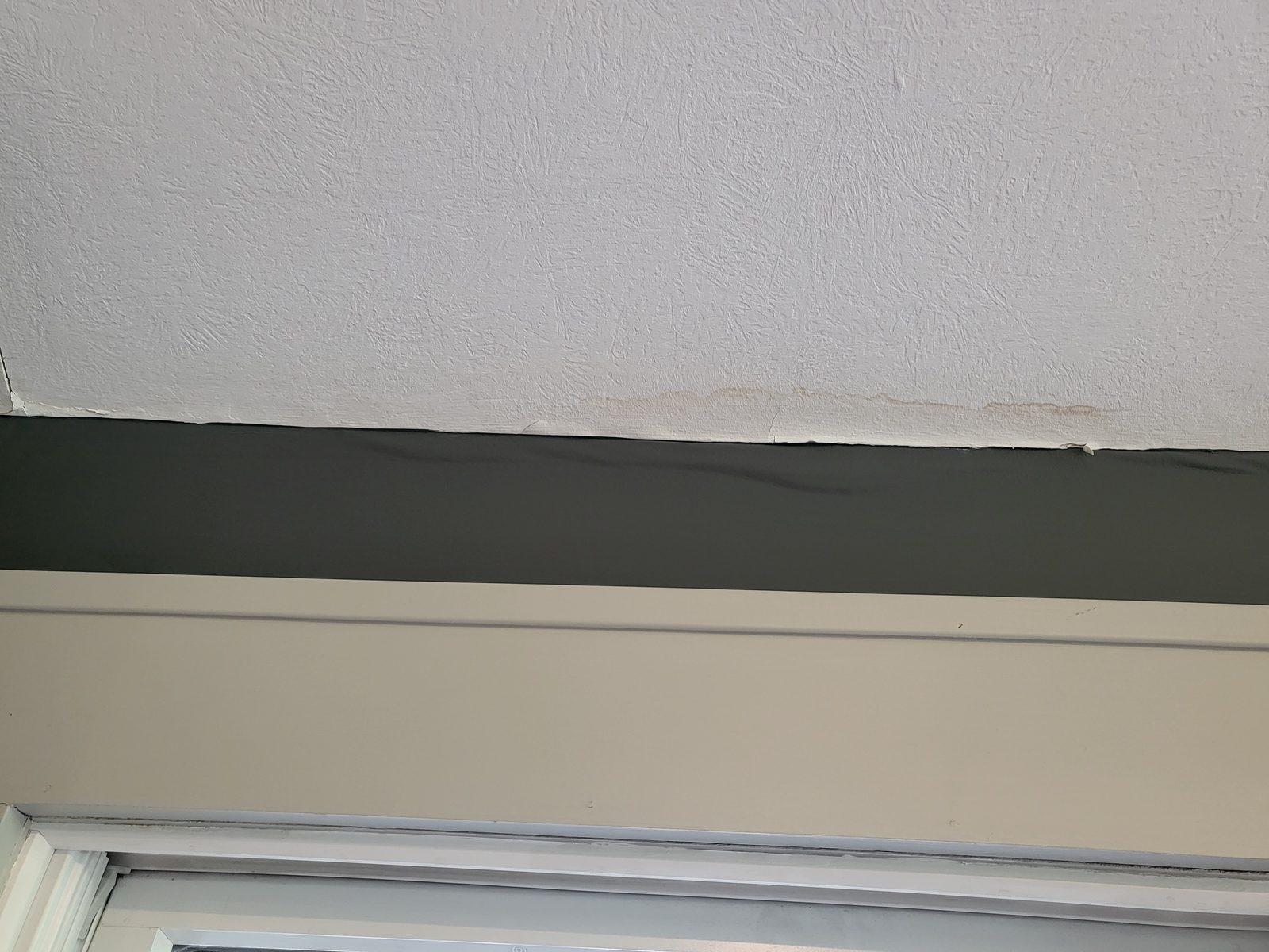 Interior ceiling-to-wall joint with paint lifting and brown water staining along the seam