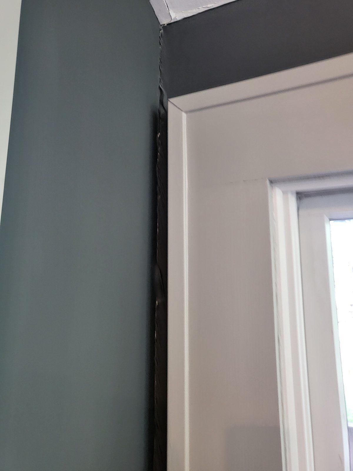 Gap opened between a door head jamb and the wall above it, with the paint line broken