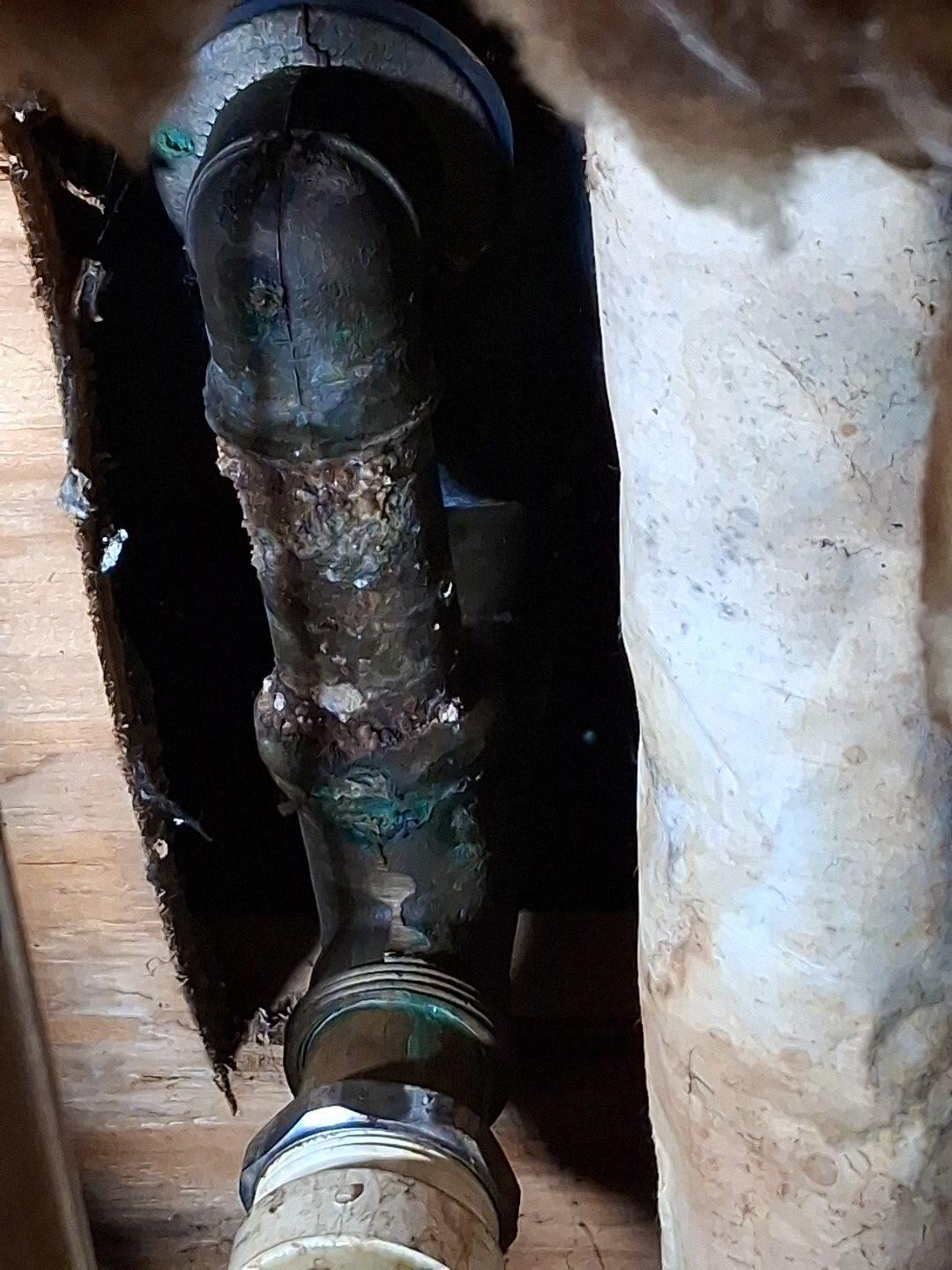 Close-up of a corroded cast-iron waste pipe with heavy green and white mineral build-up at the joint