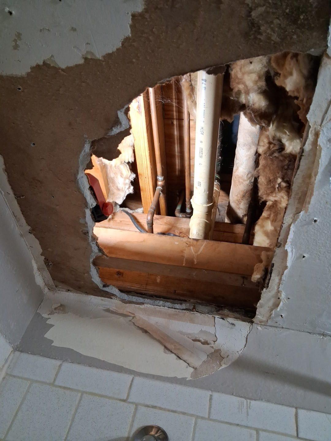 Bathroom ceiling opened up, showing joists, insulation and the waste and supply pipework above