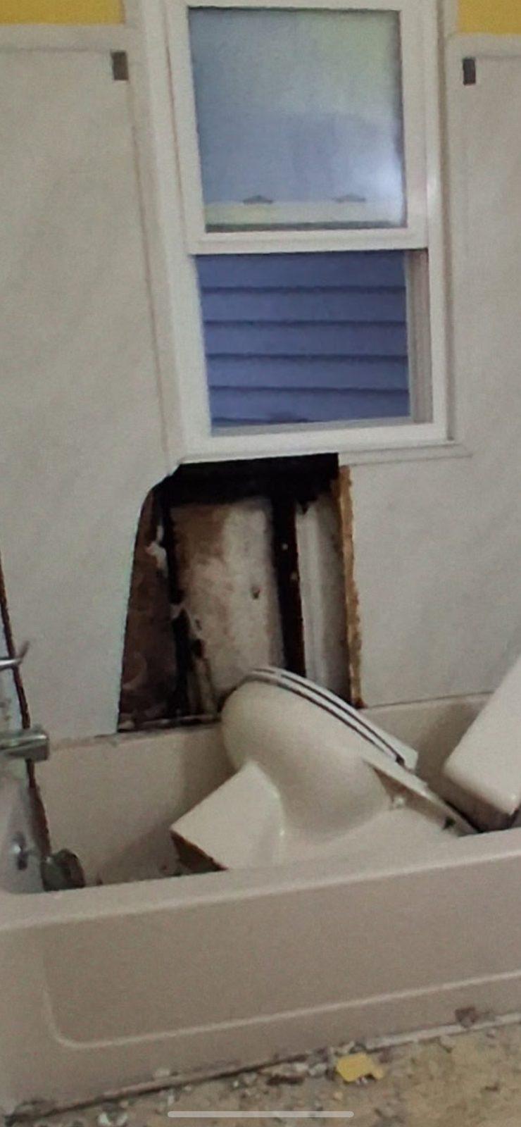 Bathroom wall opened beneath a window, showing rotted timber framing behind the removed tub surround