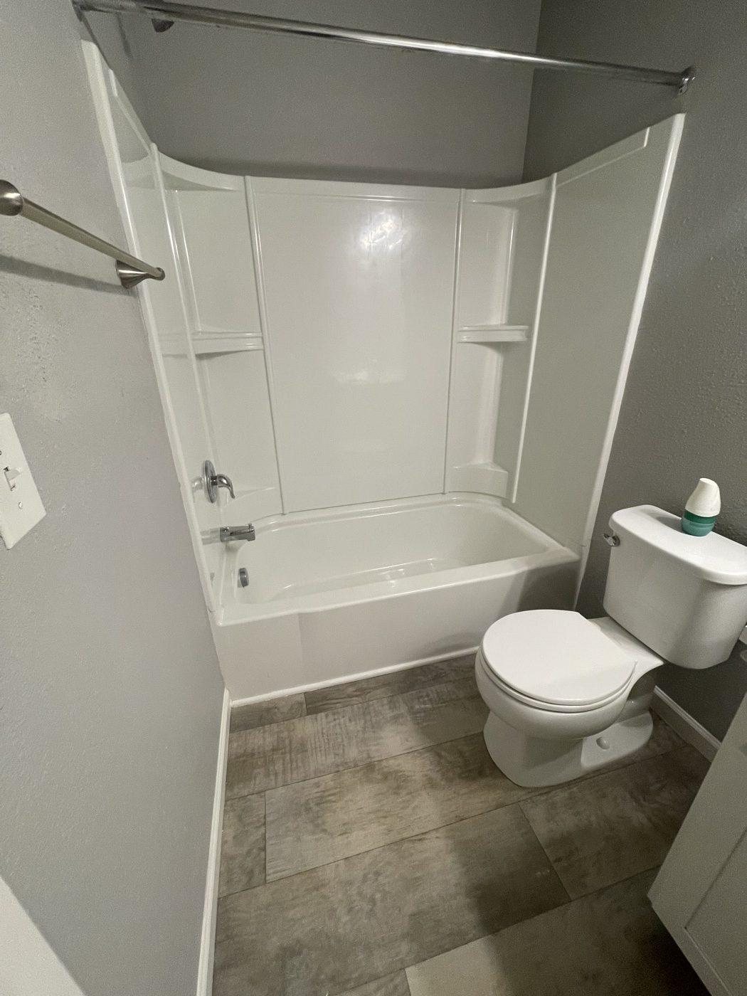 Finished rental bathroom with new tub surround, fittings, toilet and plank flooring