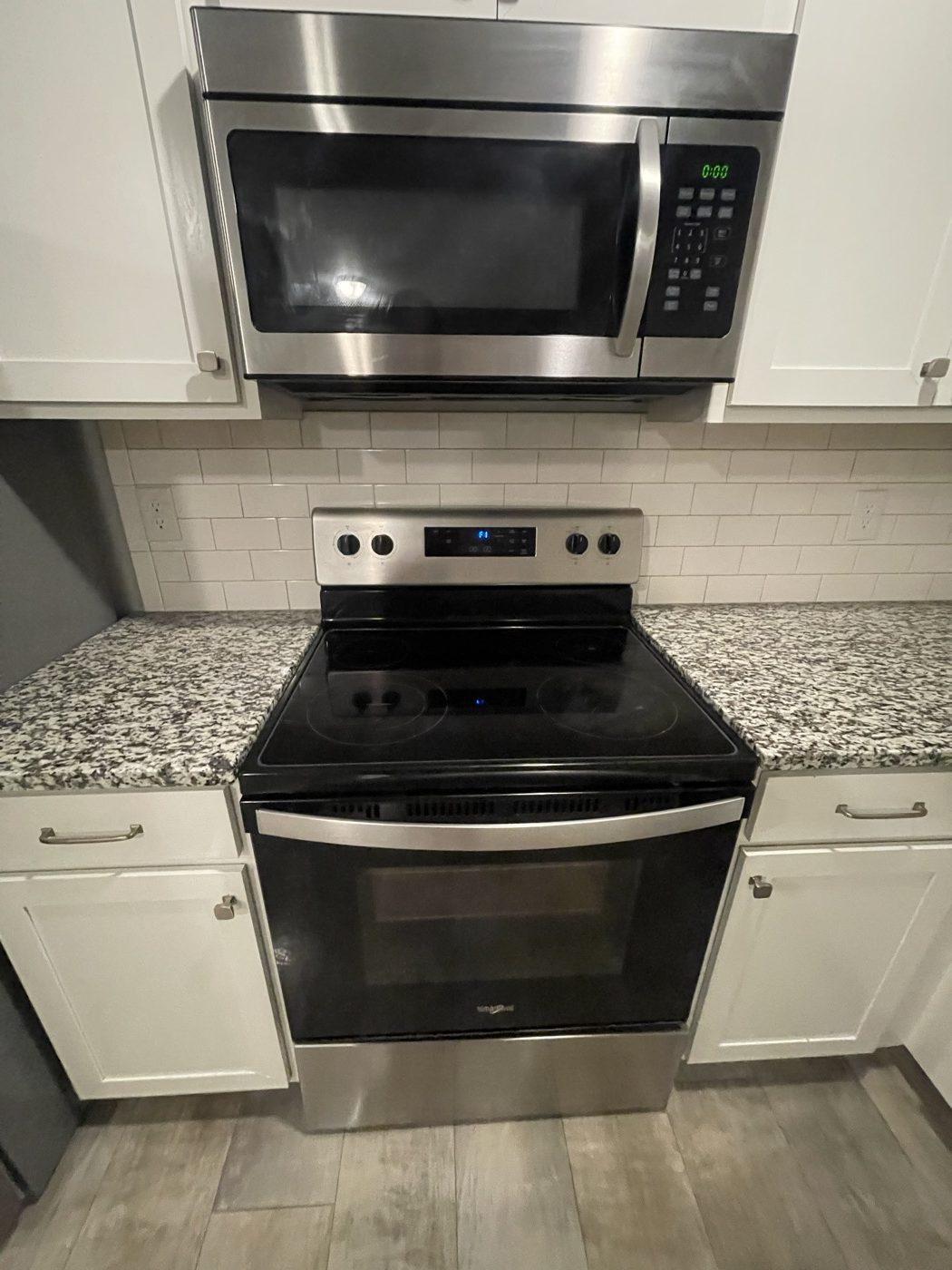 Finished rental kitchen with range, over-range microwave, tiled splashback and stone worktop